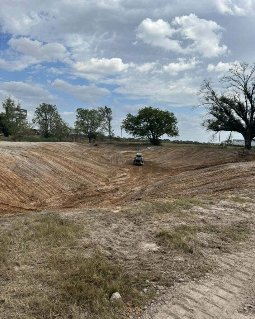 Skid steer shaping a large excavated basin as land is dug and graded for a new pond or lake
