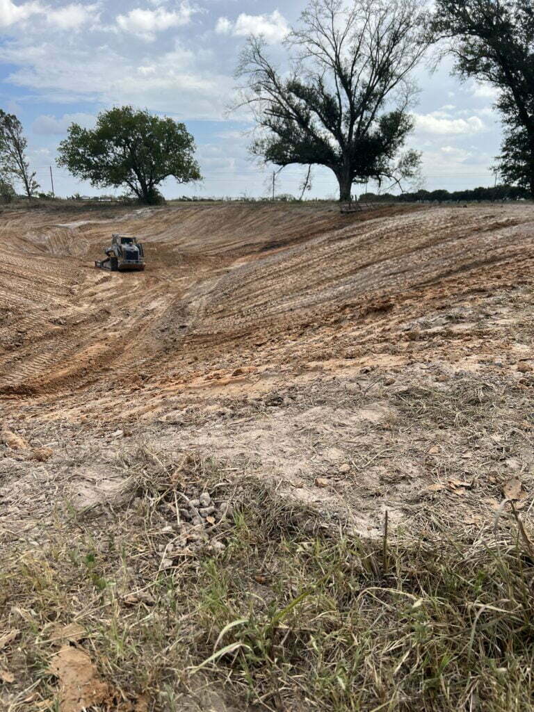 Skid steer grading a new lake basin during pond construction in Brazos County, TX