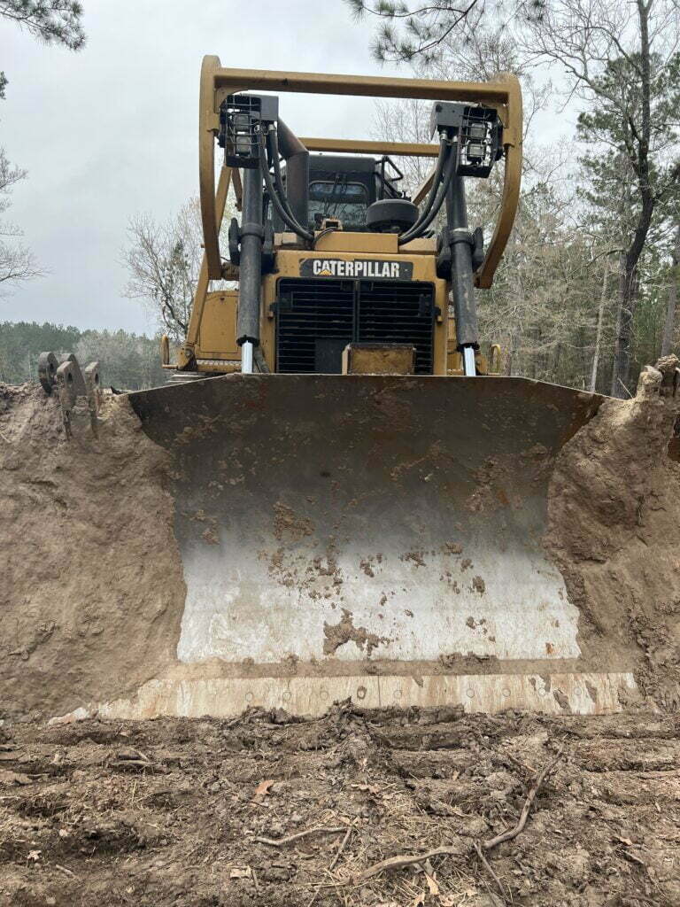 Front view of a Caterpillar dozer pushing soil for land clearing and site prep in Montgomery County, TX